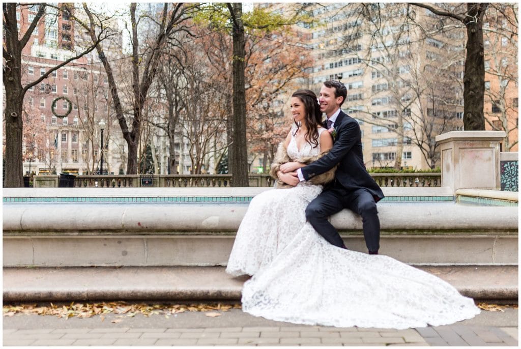 Bride and groom sit in front of fountain in Rittenhouse Square Park at winter holiday wedding