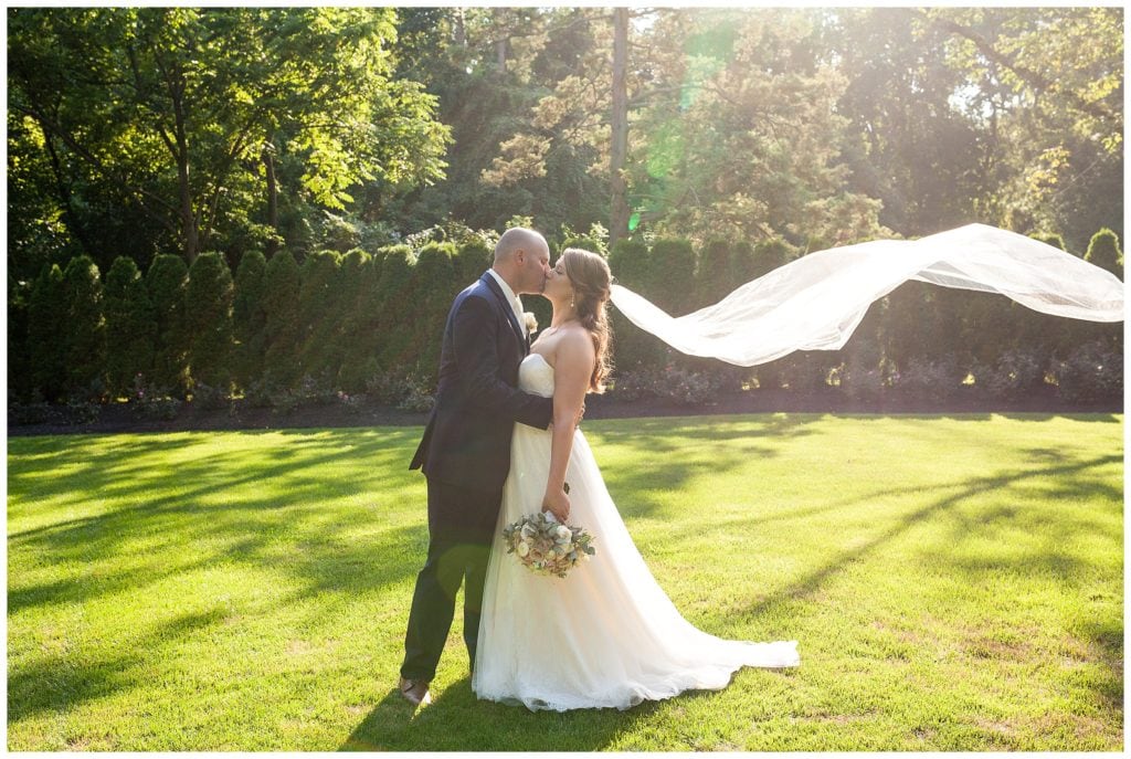 Bride and groom kissing in garden with long veil flowing in the wind