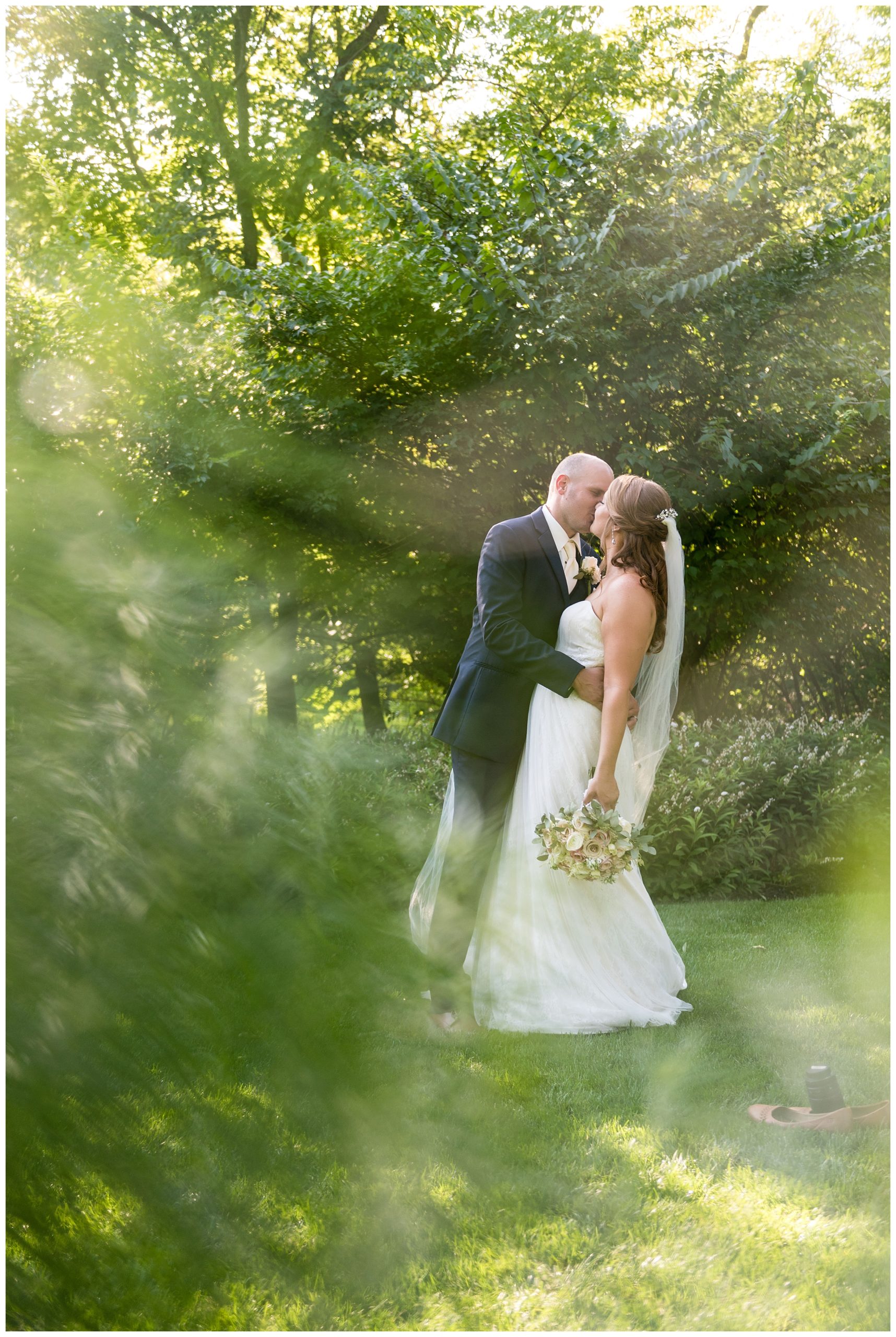 Bride and groom kissing in gardens shot through leaves