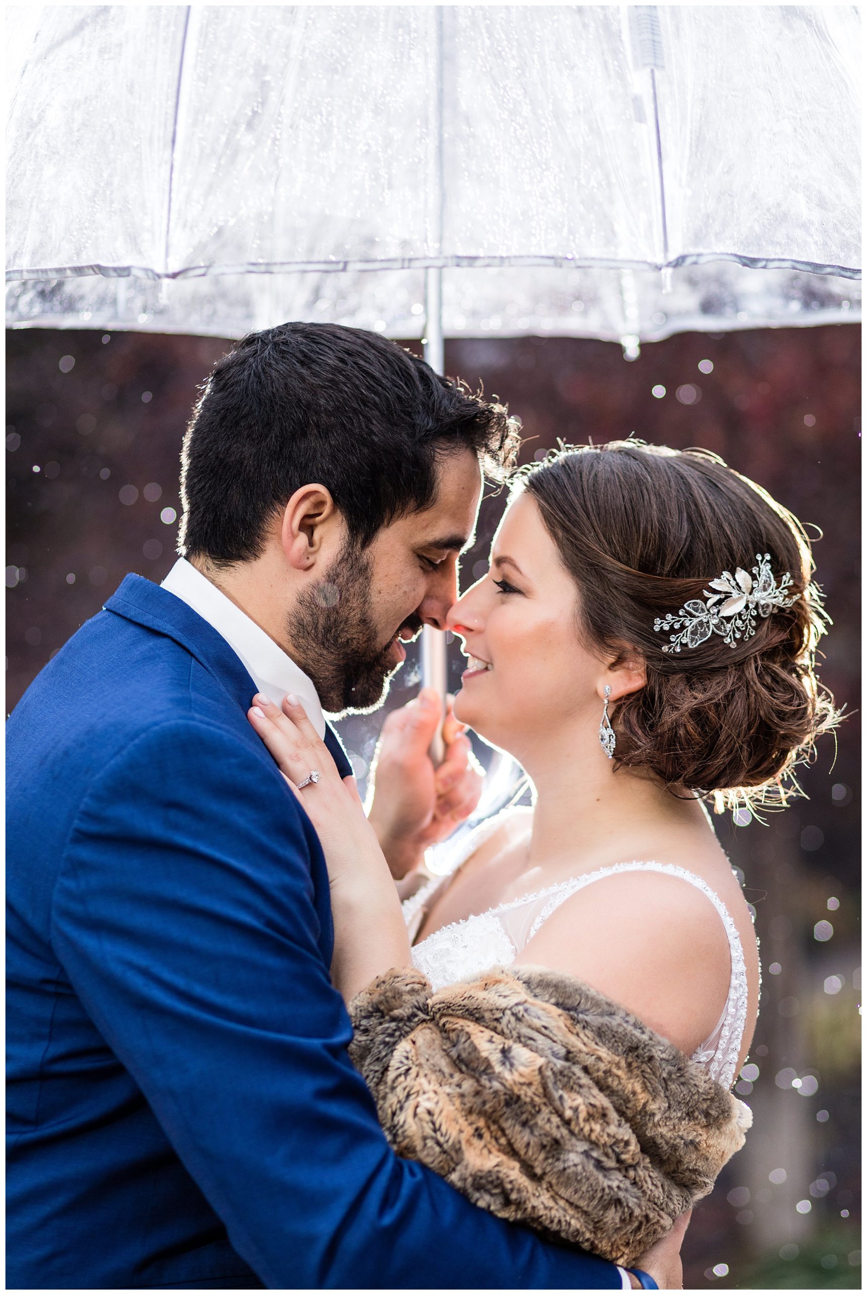 Bride and groom snuggle under umbrella in snow at Radnor Hotel winter wedding