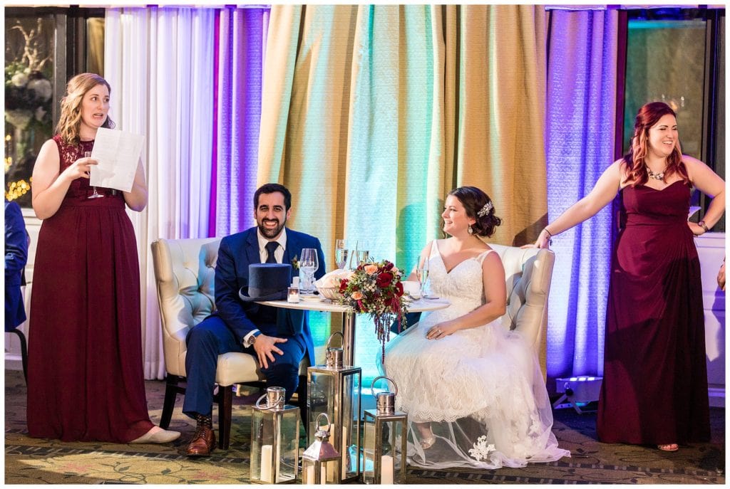 Bride and groom at sweetheart table listening and laughing at speeches from maids of honor at Radnor hotel winter wedding reception