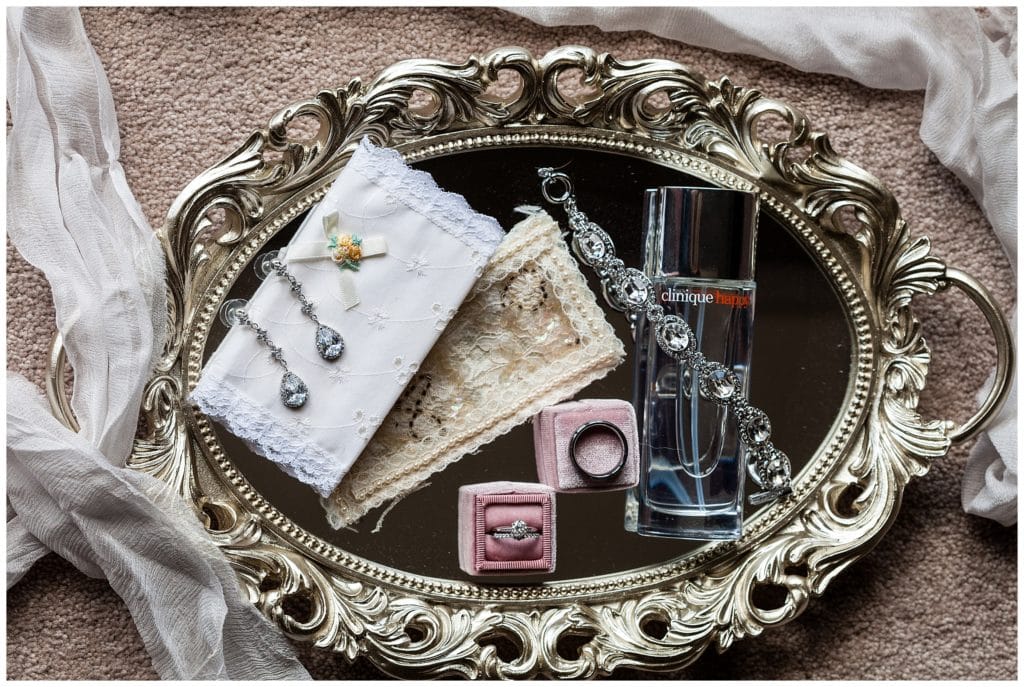 Bridal detail tray with earrings, engagement ring and wedding bands, perfume, bracelet, and handkerchiefs