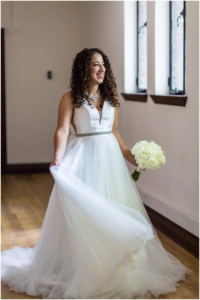 Window lit portrait of bride fluffing her tulle dress