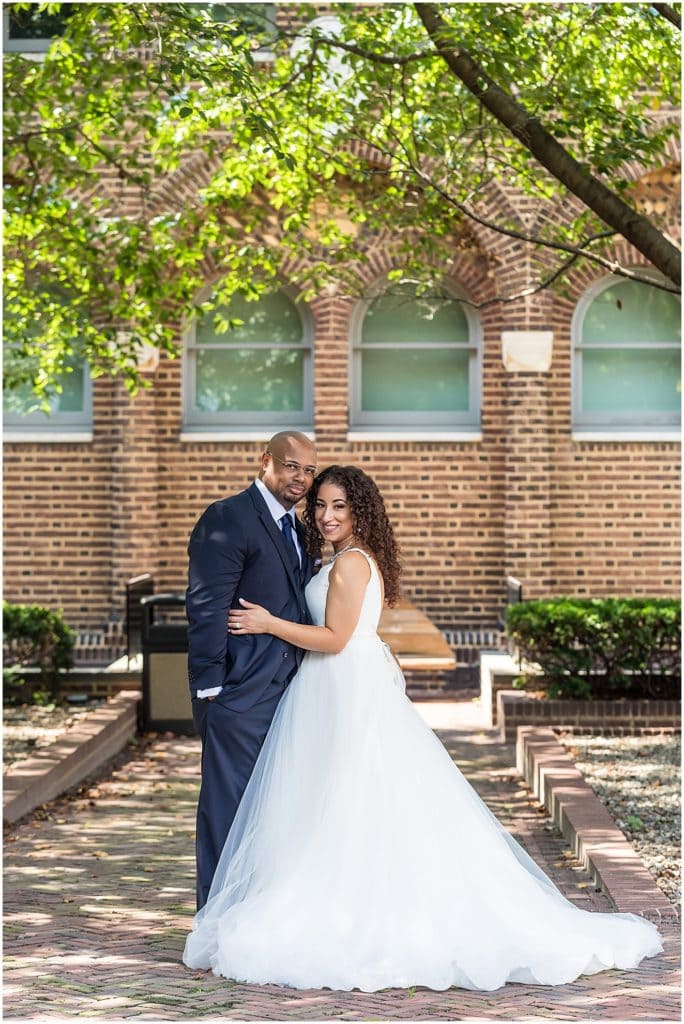 Bride hugs groom around waist in Penn Museum garden courtyard wedding portrait