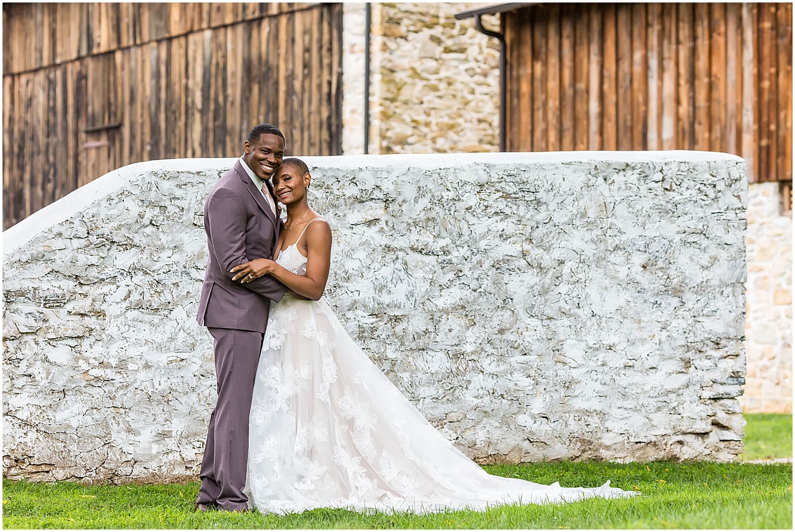 Bride and groom hug close in front of barns at Duportail House wedding