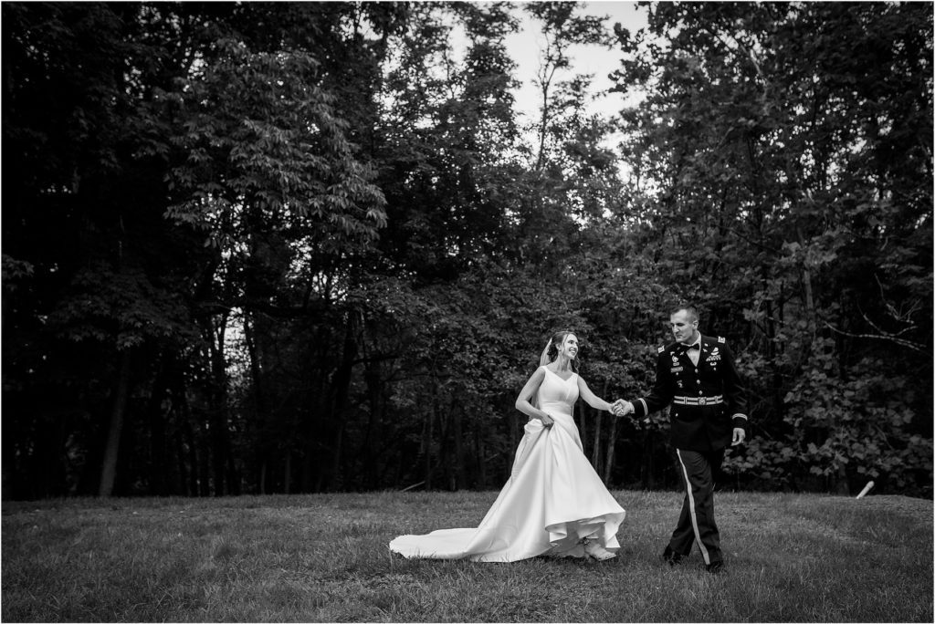 Black and white portrait of bride and military groom walking hand in hand through a field in Lehigh Valley wedding