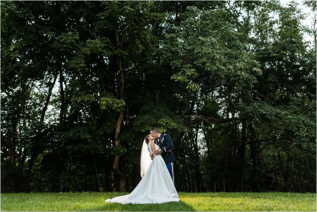 Backlit portrait of groom dipping and kissing bride in front of tree line at Lehigh Valley wedding