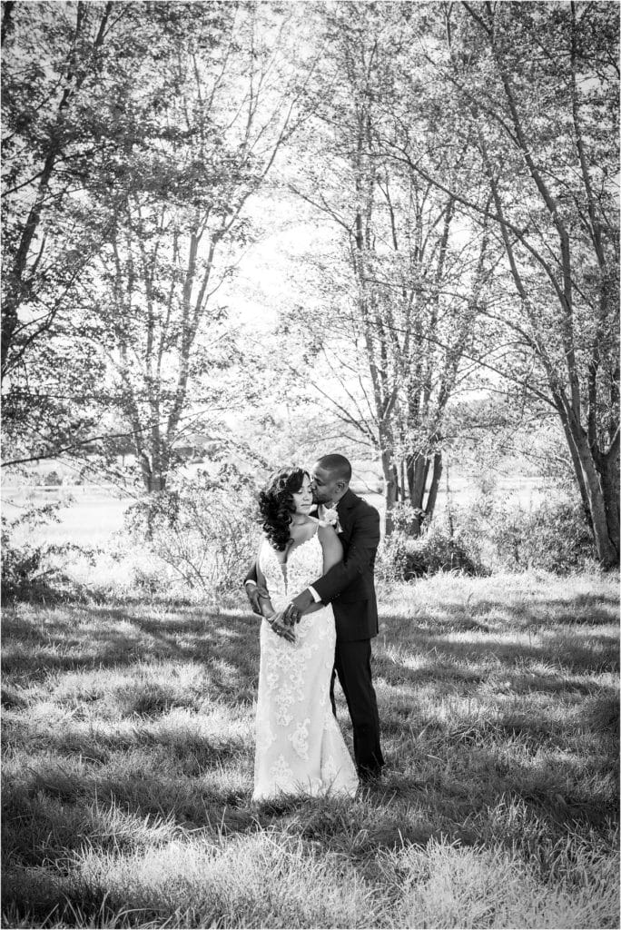 Black and white portrait of husband kissing wife on cheek in field at Barn at Stoneybrooke 25th wedding anniversary