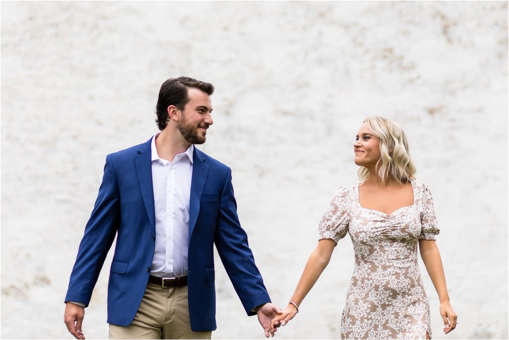 couple holds hands and walks through Valley Forge Park at engagement session