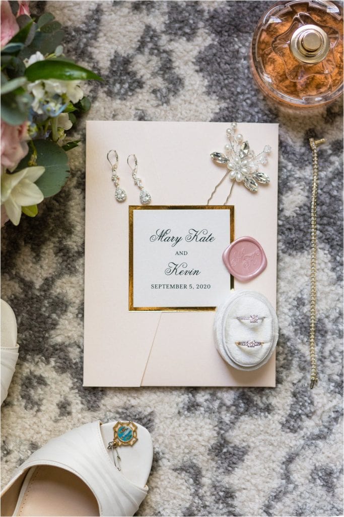 Simple white and gold wedding invitation with earrings, hair pin, engagement ring, perfume, and charm details
