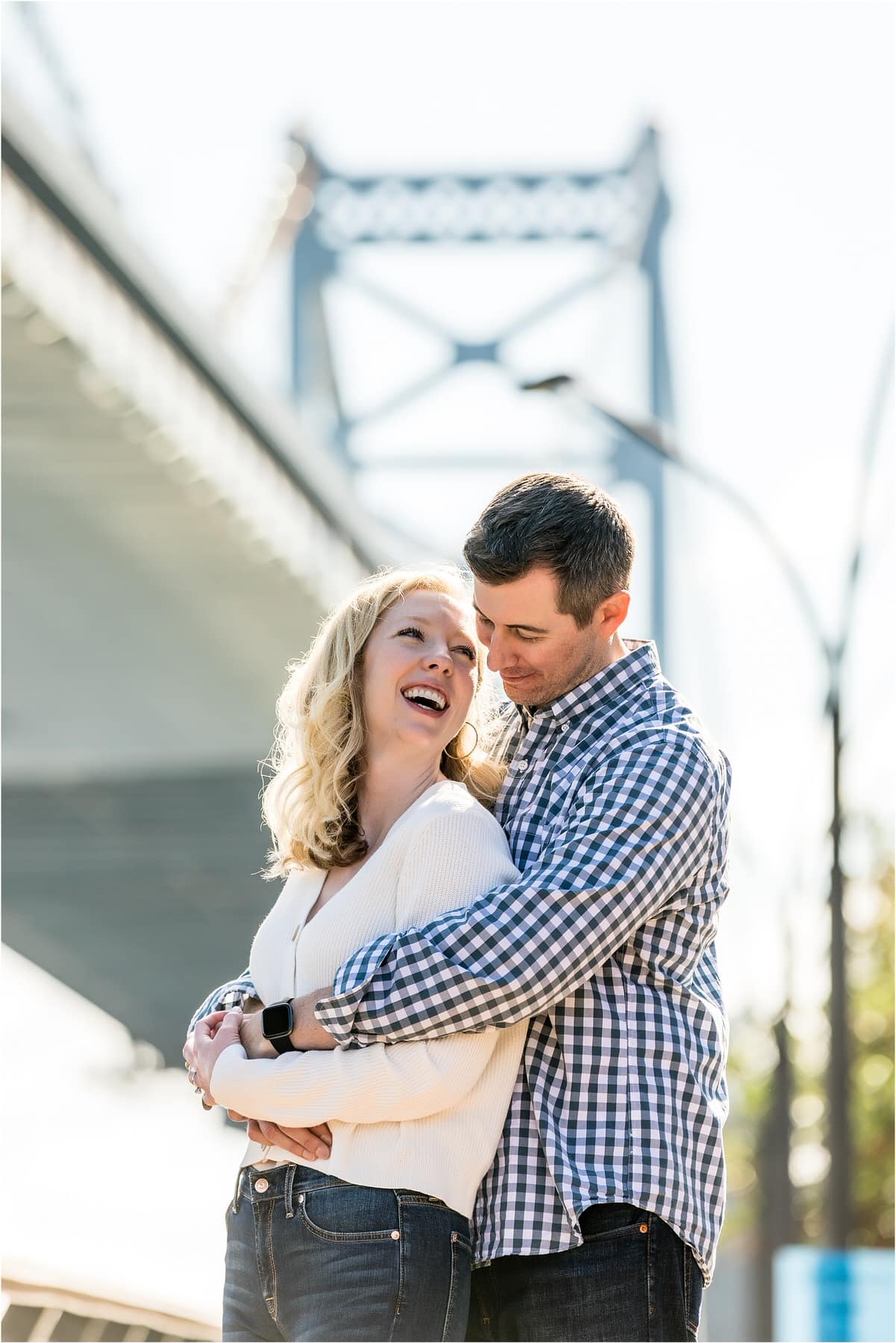 Romantic engagement portrait of couple hugging and laughing under bridge on Race Street Pier in Old City Philadelphia engagement session