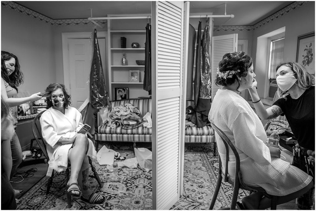 Black and white portrait of two brides getting hair and makeup done in bridal suite across room divider at same sex pride wedding