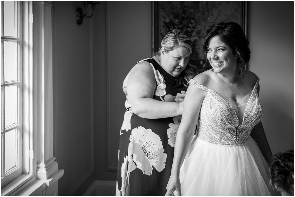 Black and white portrait of smiling bride getting her gown buttoned