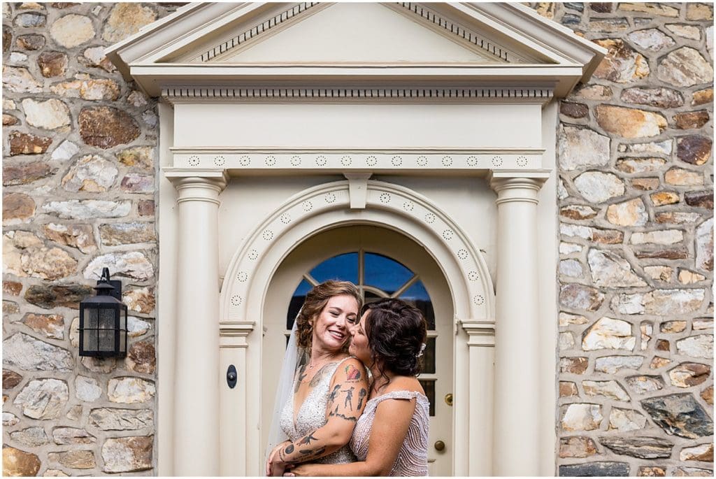 Lesbian brides hug around waist and smile at each other in front of arch doorway