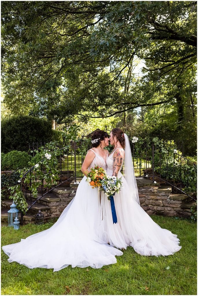 Brides kiss and hold orange and blue bouquets together in gardens at Bolingbroke Mansion Pride wedding