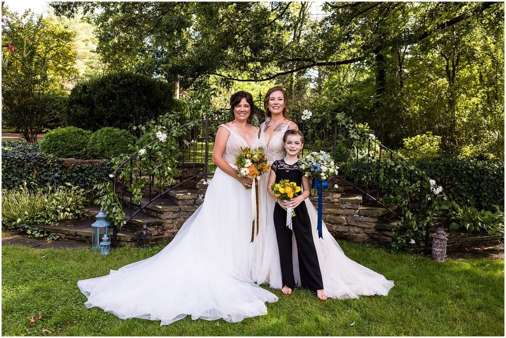 Brides stand with their daughter in gardens of Bolingbroke Mansion at same sex Pride wedding