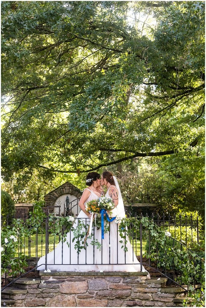 Brides kiss on stone stairway in gardens at Bolingbroke Mansion pride wedding