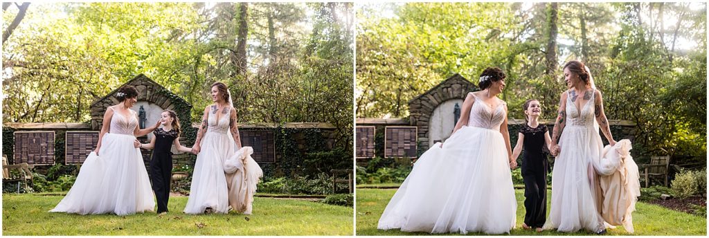 Brides hold hands with daughter and walk through gardens at Bolingbroke Mansion pride wedding