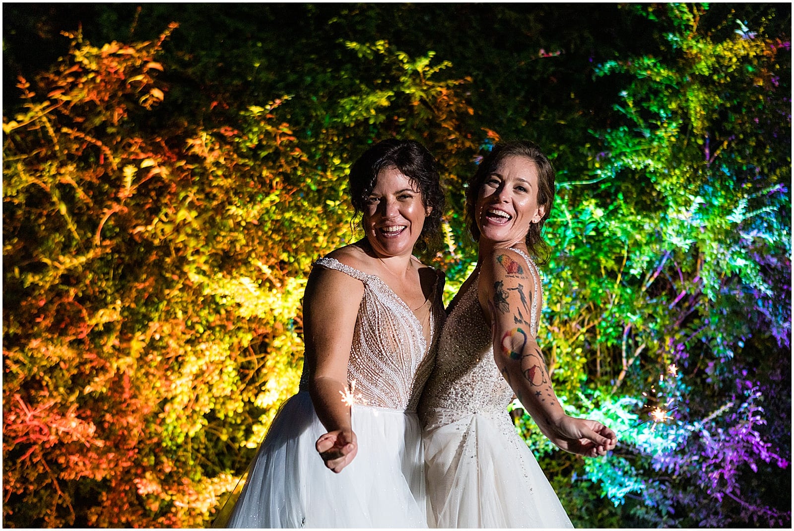 Brides light sparklers in front of rainbow lit trees at Bolingbroke Mansion same sex Pride wedding