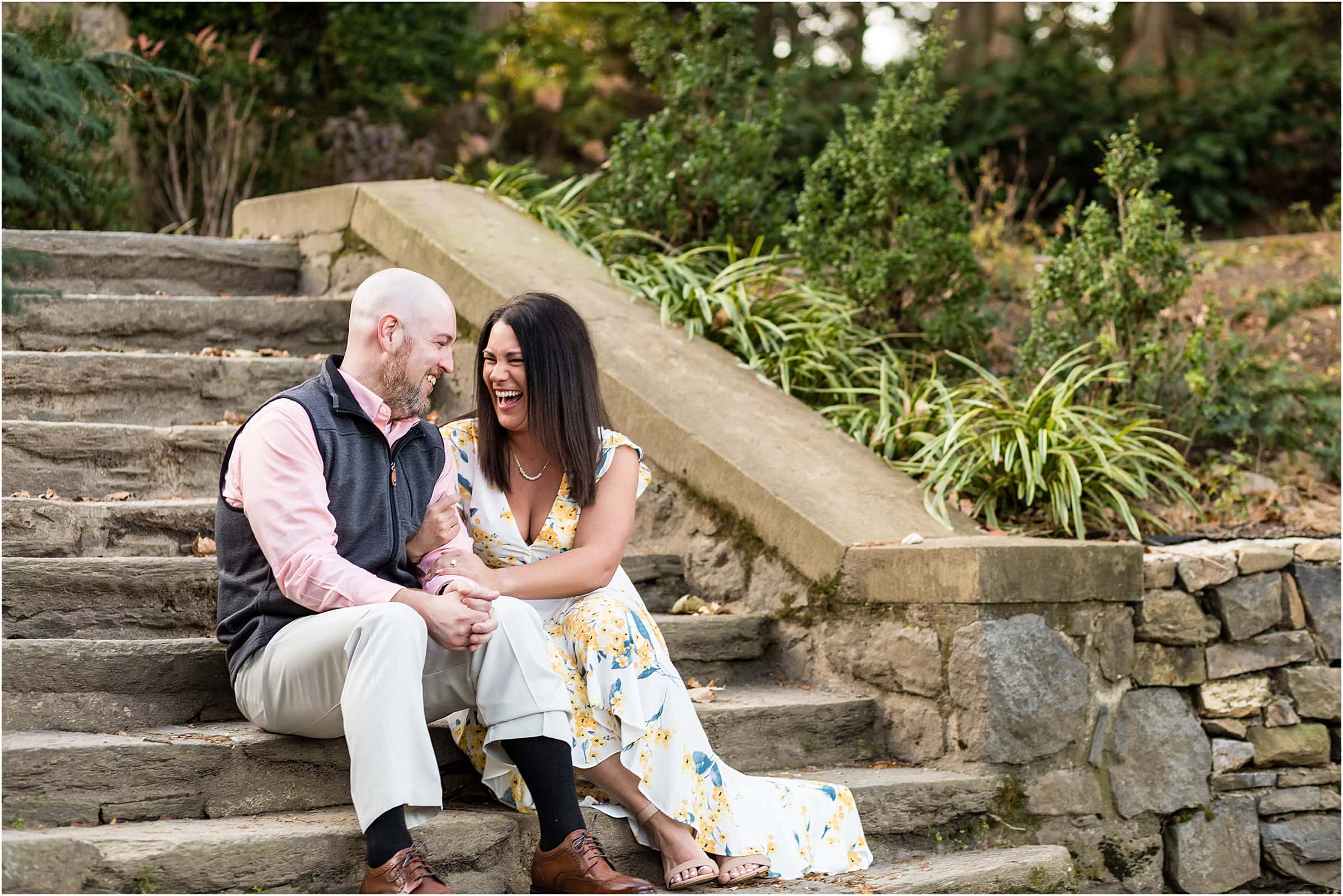 Couple sitting on stone staircase and laughing with each other at Ridley Creek Park engagement session