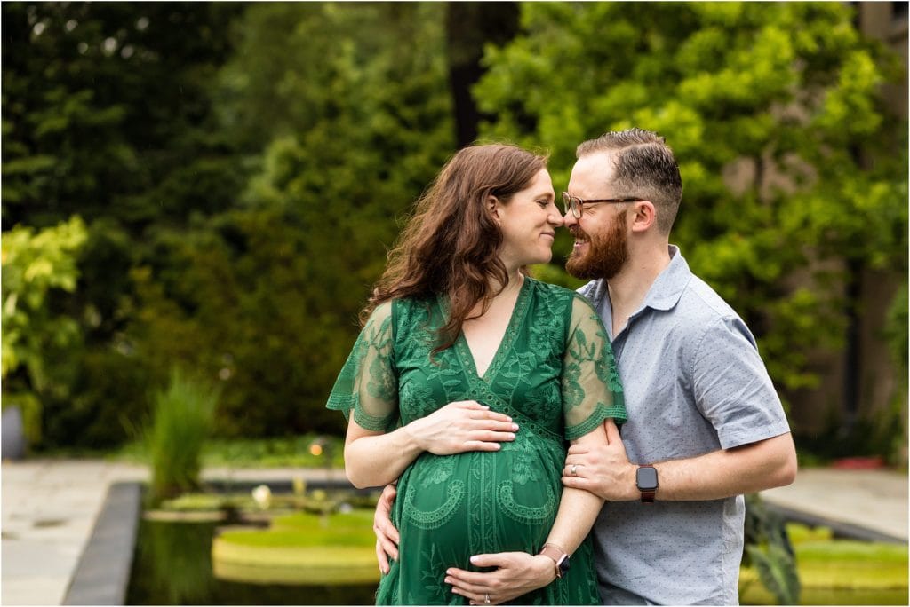 Husband and wife pulling apart from a kiss in front of lily pad pond at Longwood Gardens maternity session