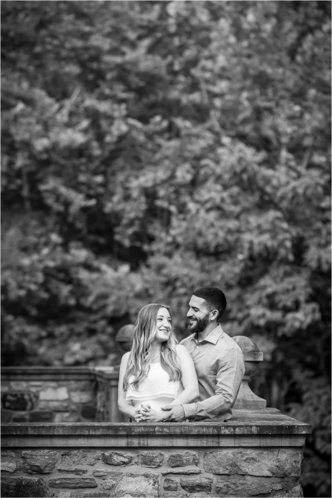 summer ridley creek engagement session - black and white image of couple smiling behind a stone wall | Ashley Gerrity Photography
