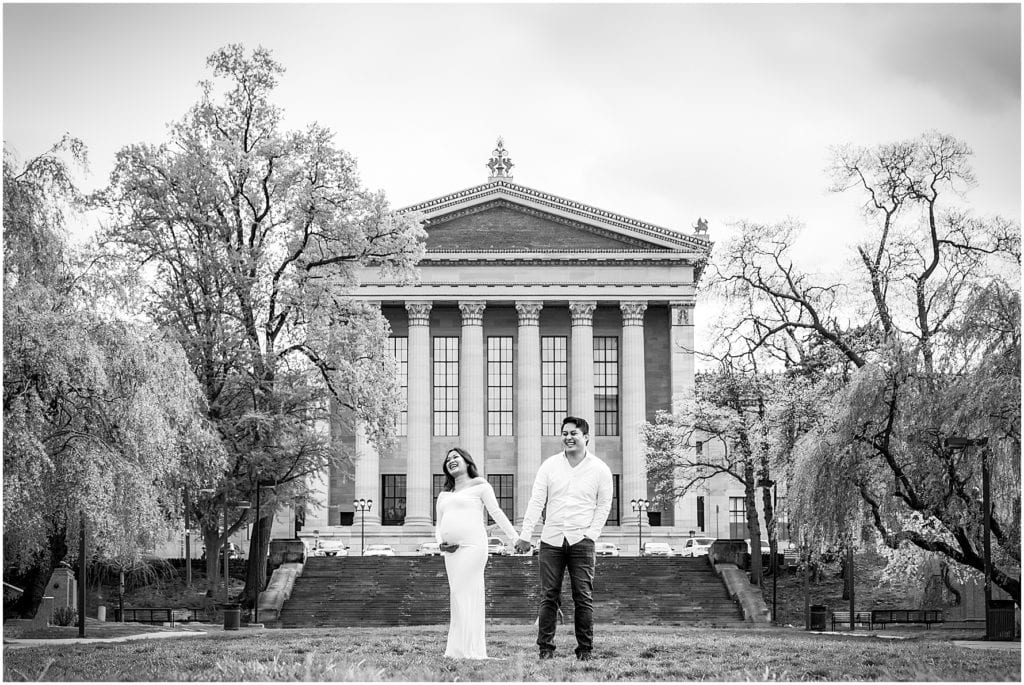 Black and white maternity session portrait of husband and wife laughing in front of Philadelphia Art Museum