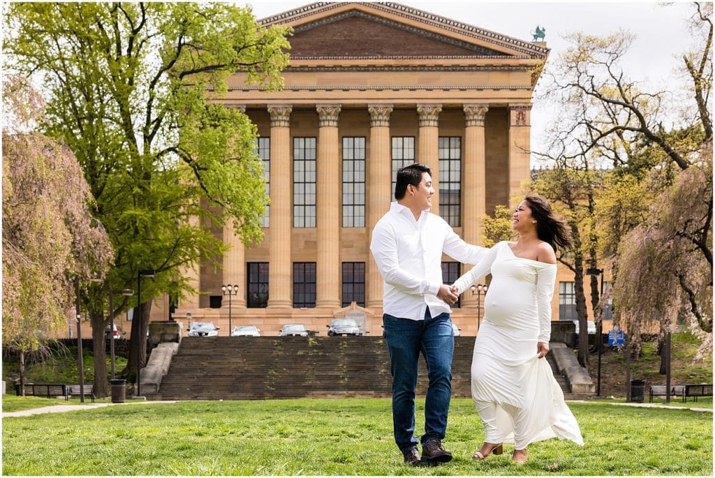 Husband and wife walking hand in hand in front of Philadelphia Art Museum maternity session