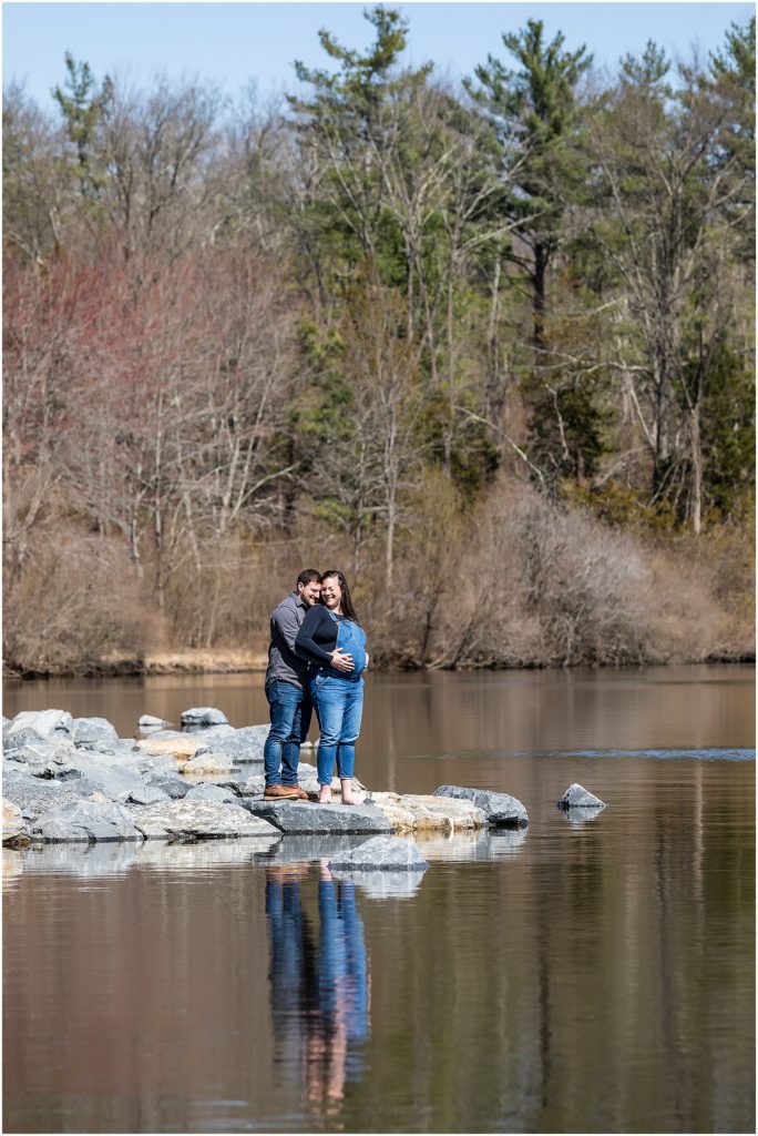 Husband and wife stand on rock edge of lake in Pocono Mountain maternity session