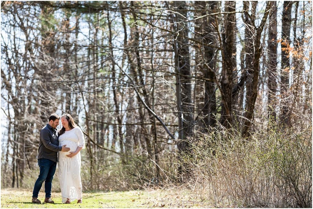 Pocono Mountain maternity session portrait of husband and wife laughing while holding baby belly