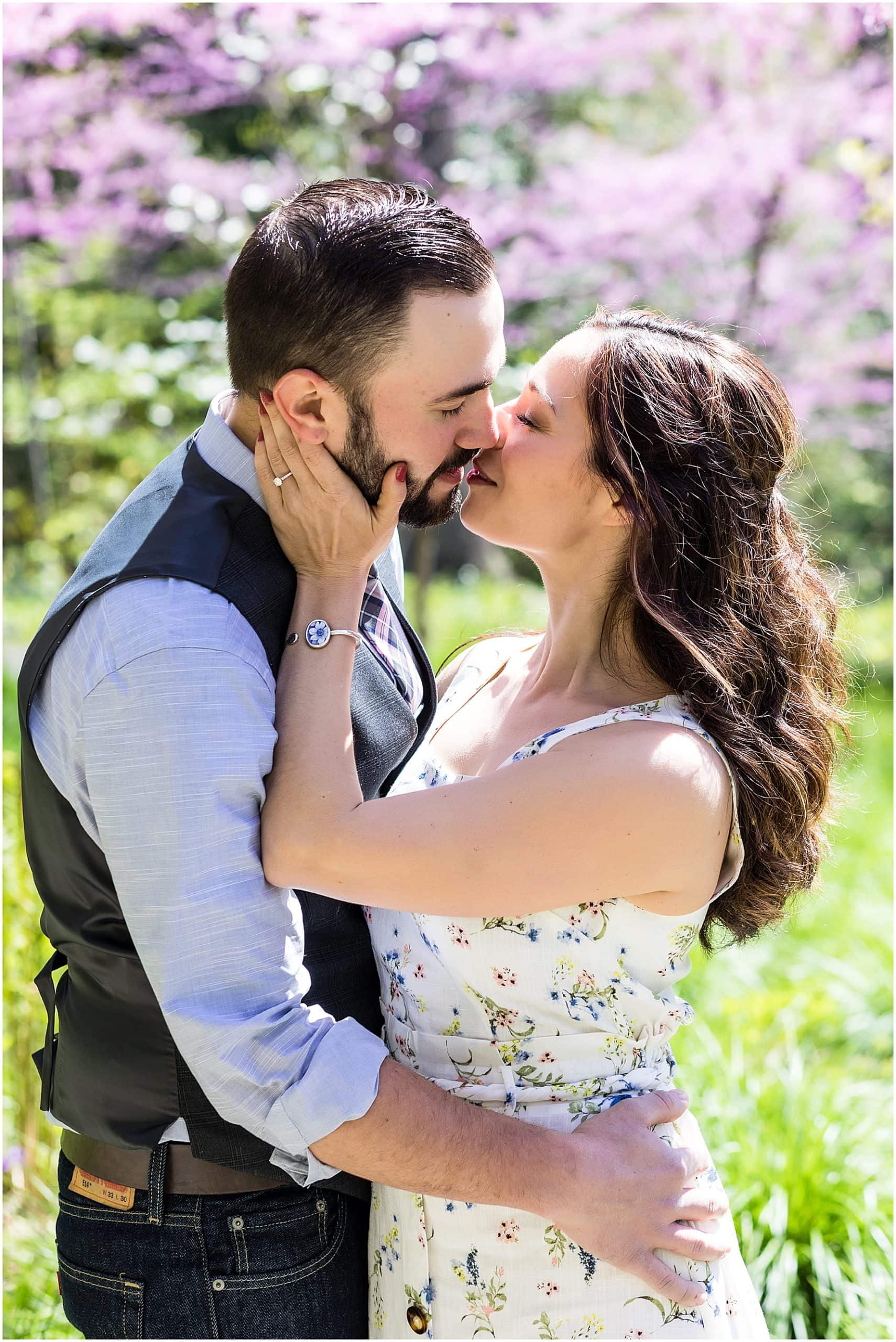 Couple pulling apart from a kiss in front of pink trees at Longwood Gardens engagement session