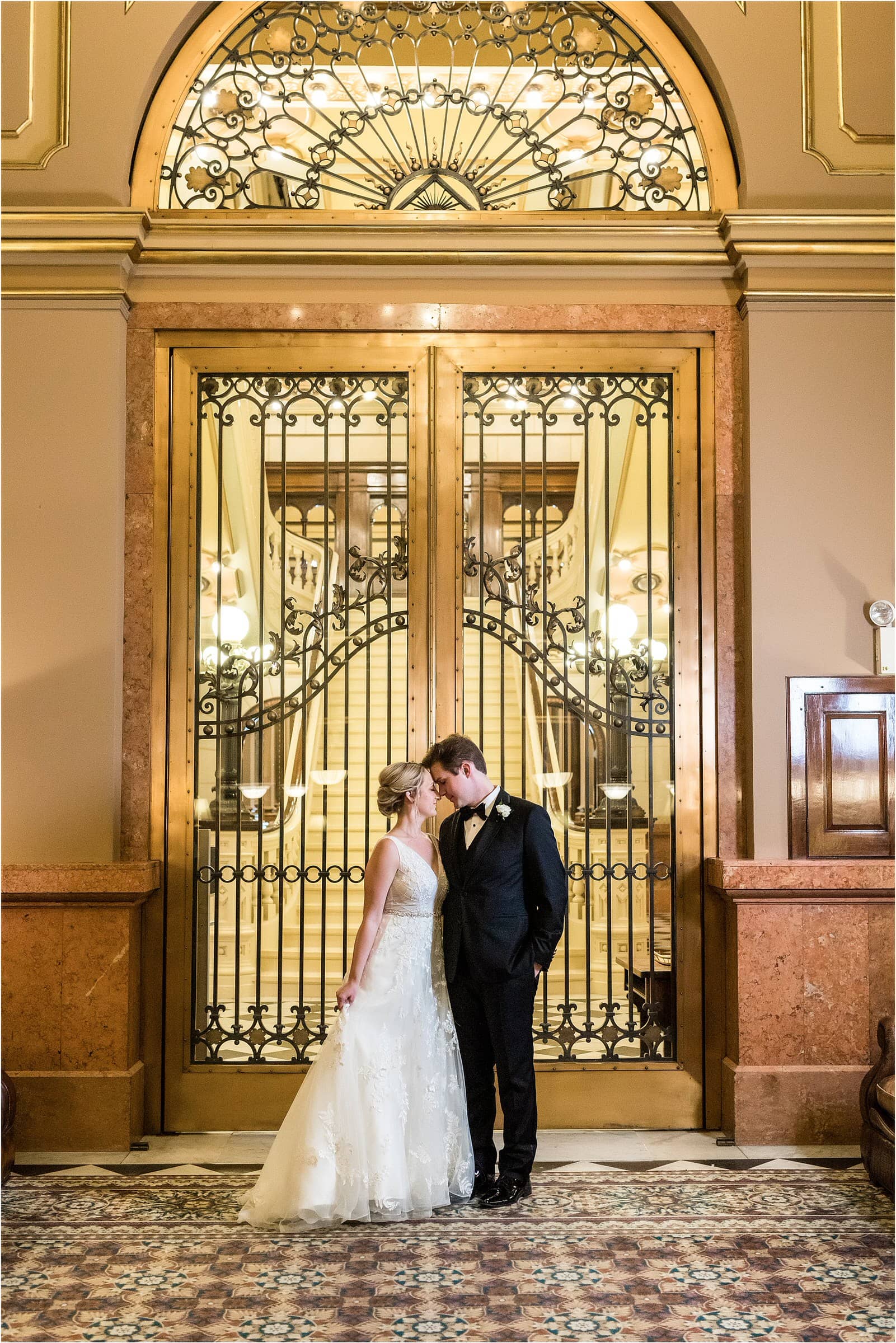 The bride and groom touching foreheads and leaning in close up against a gold doorway