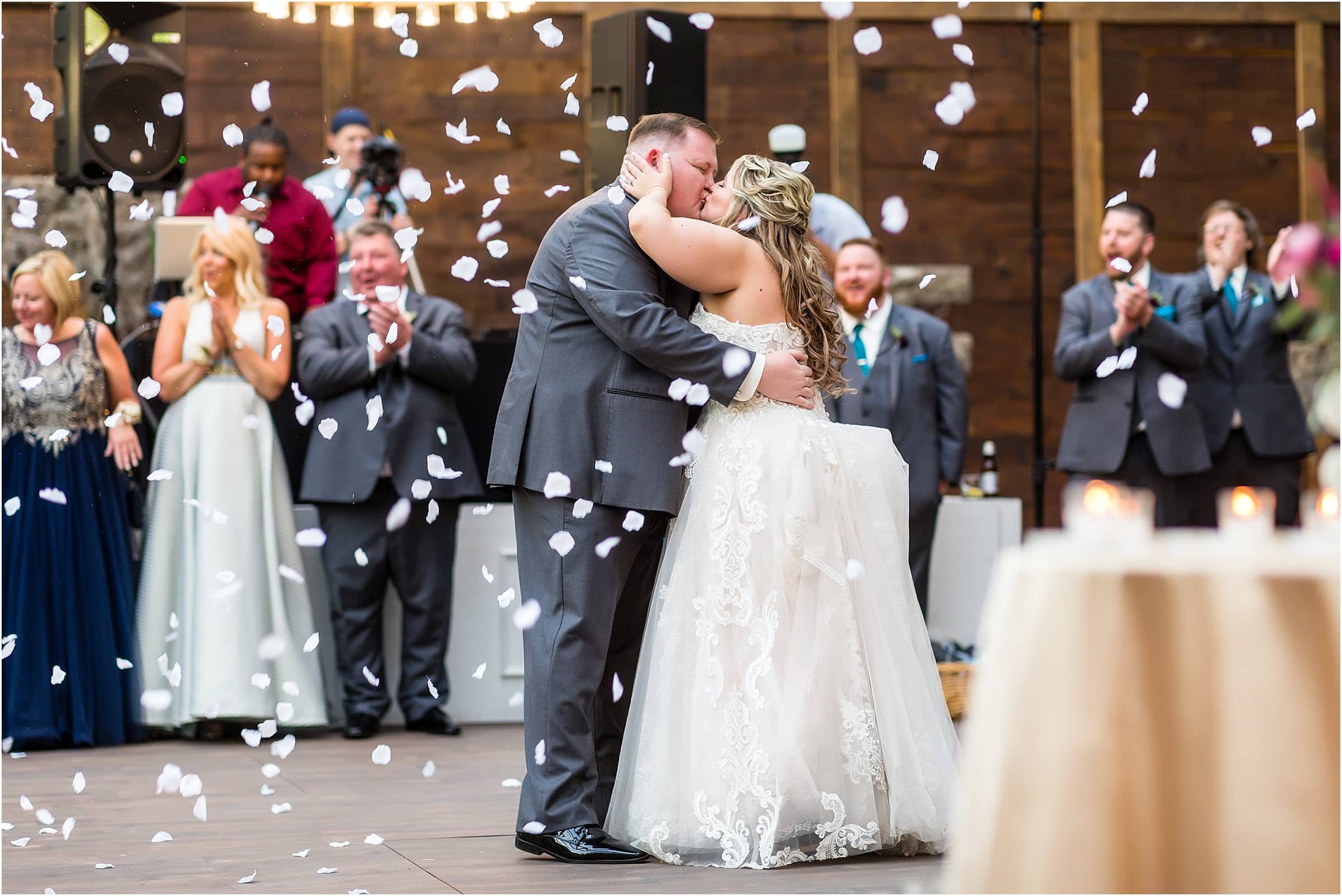Bride and groom kissing during first dance as pedals fall around them