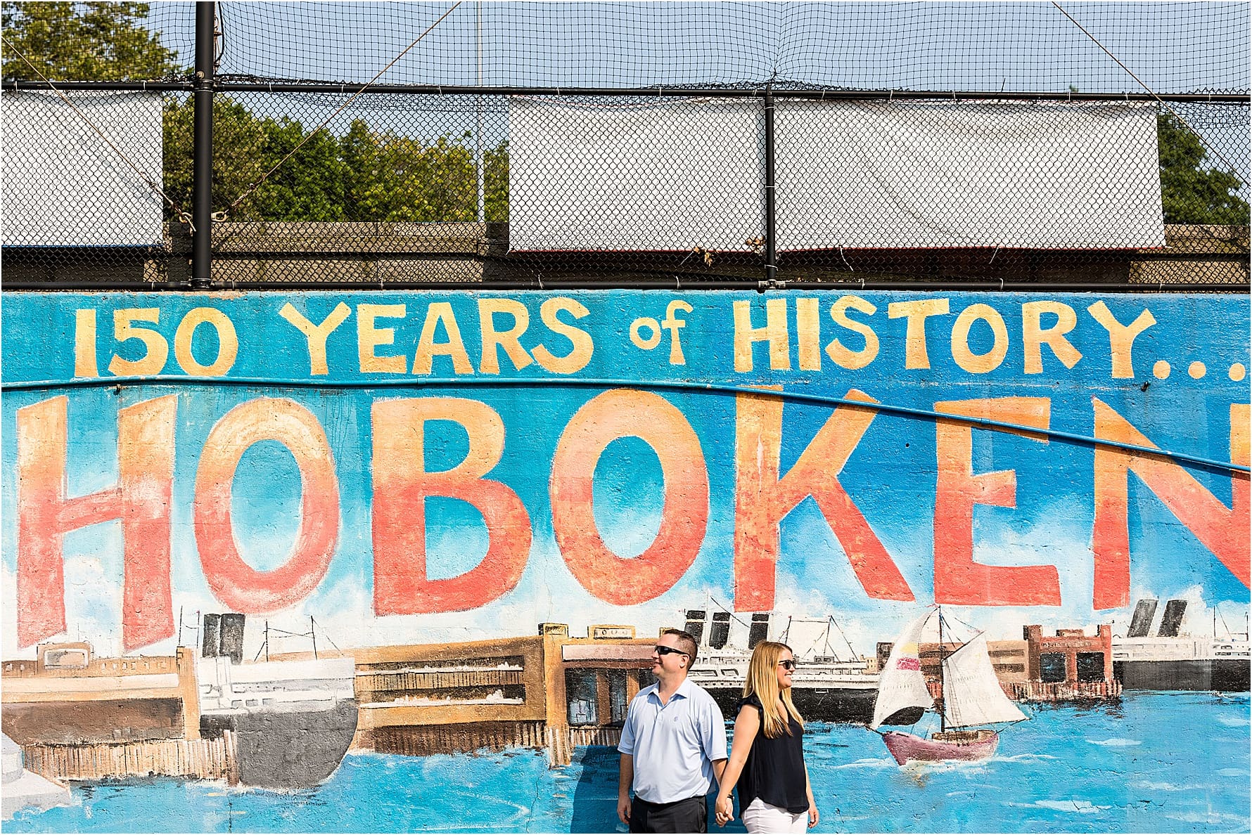Bride and groom holding hands facing away from one another in front of a Hoboken painting