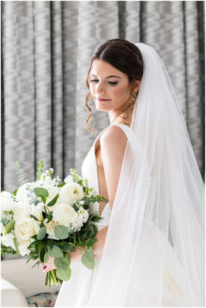 Bride looks over her shoulder, holding her bouquet, as she stands in her wedding dress and veil 
