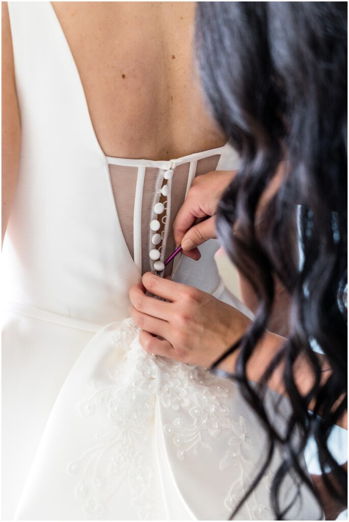 Rows of buttons at the back of a wedding gown are carefully buttoned