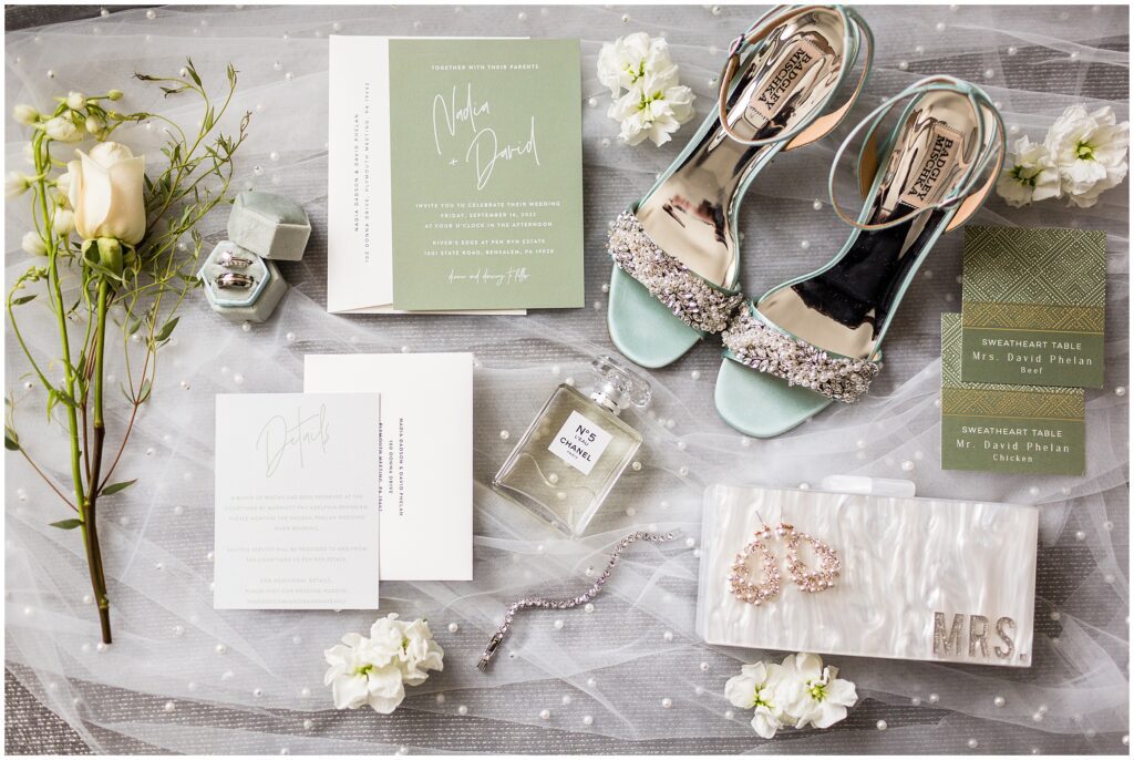 wedding stationery featuring green paper with white text, seating cards with green patterned paper, wedding bands, blue bridal shoes, and other bridal accessories