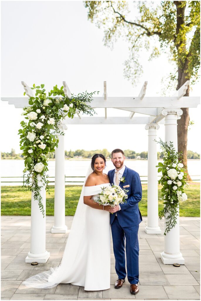 Bride and Groom stand near white structure with white florals