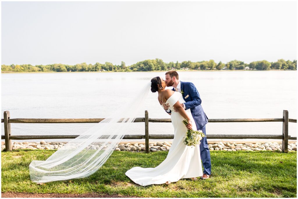 Groom dips bride while kissing, and bride's veil is carried gracefully behind her by the wind