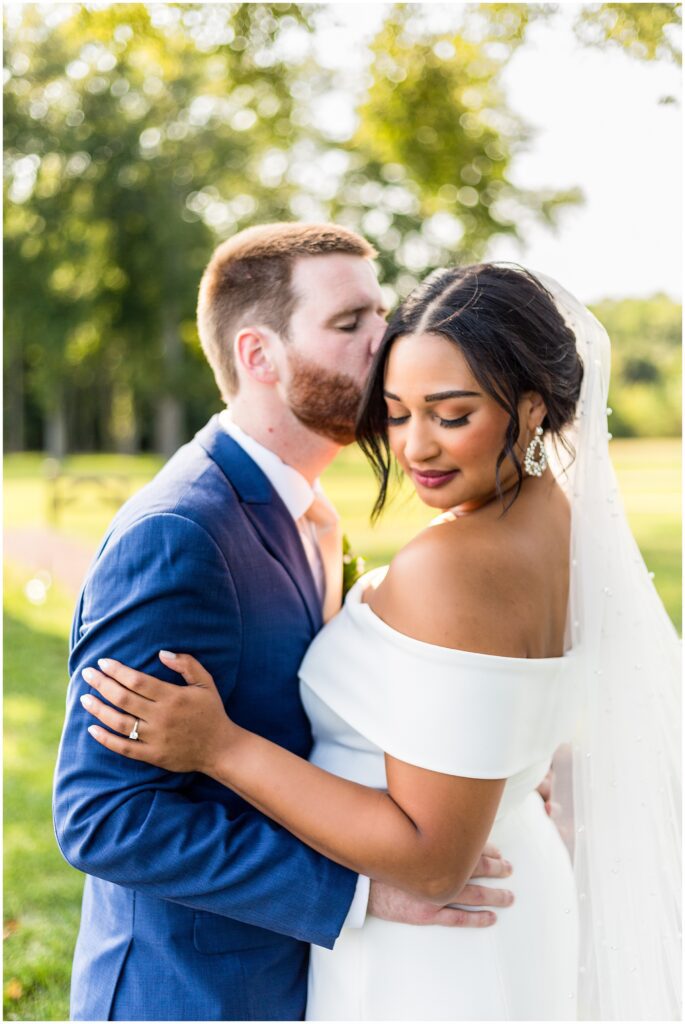 portrait of bride in white off the shoulder dress with groom in navy suit kissing her