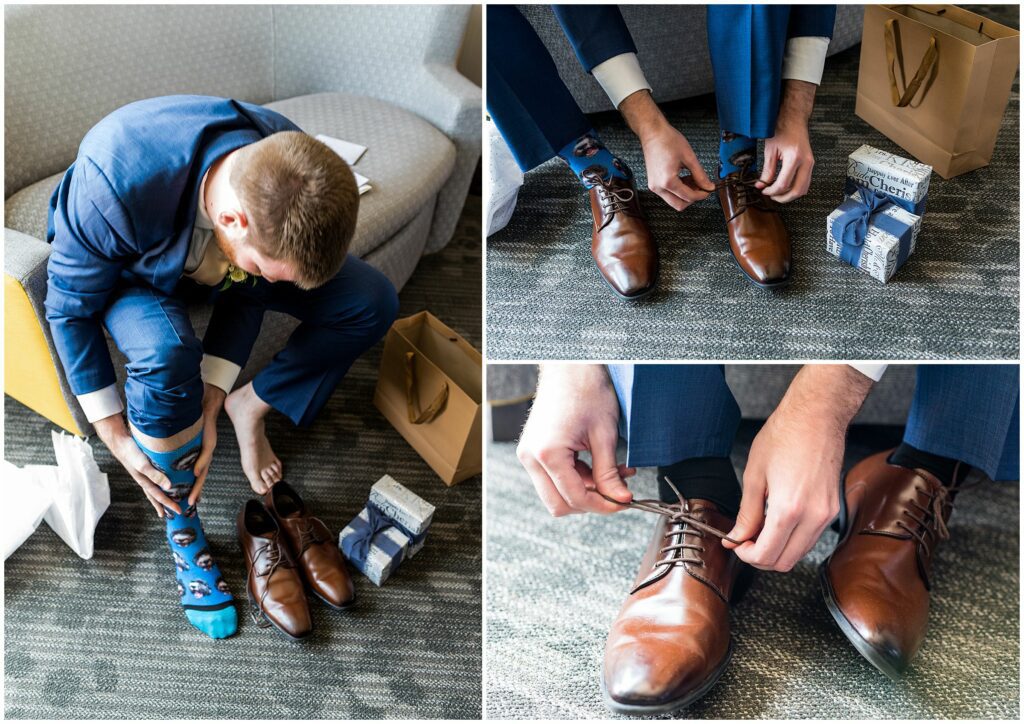Groom puts on his fun socks, and ties his brown shoes. Two small boxes that are wrapped with blue ribbons are next to his feet.