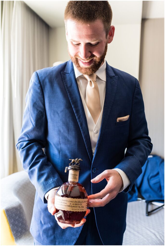 Groom holds bottle of whiskey while getting ready for wedding