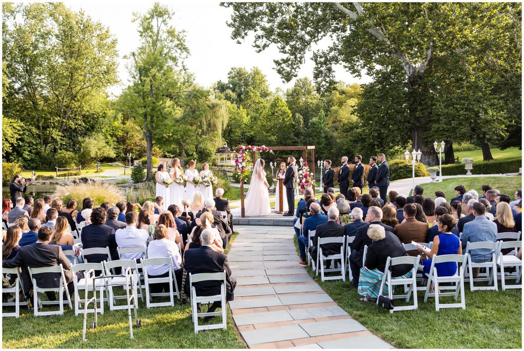 Outdoor wedding ceremony with couple standing under chuppah with pink florals