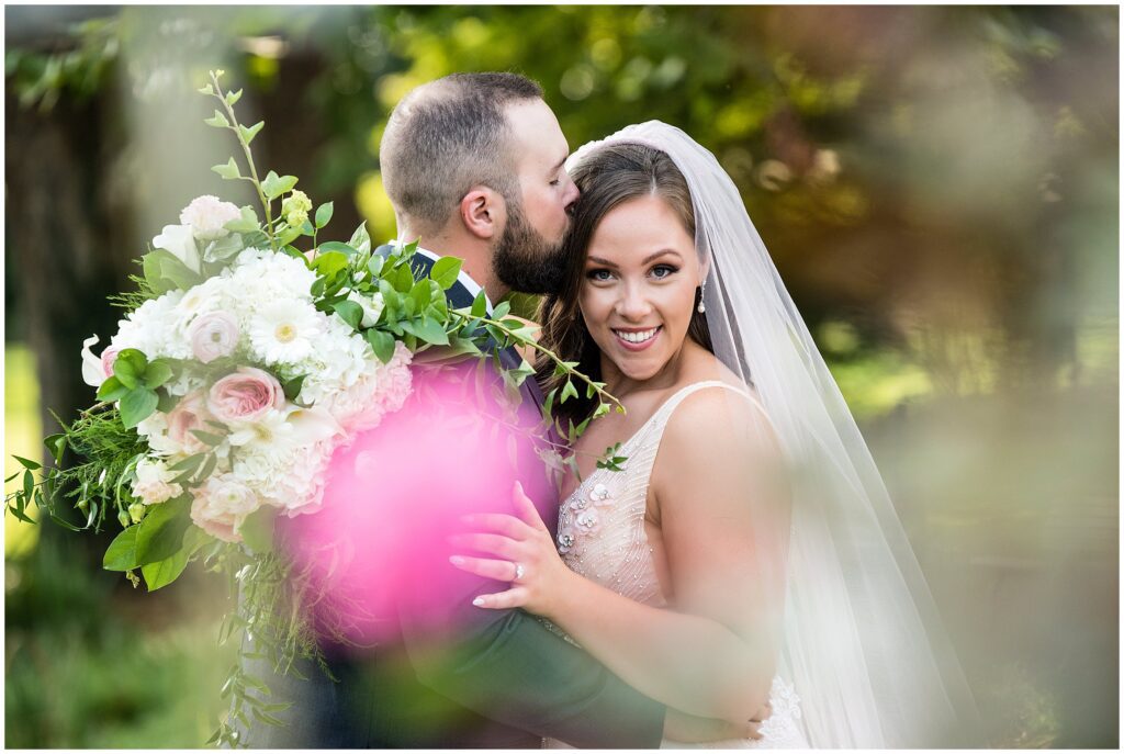 Groom kisses his bride as she smiles towards camera