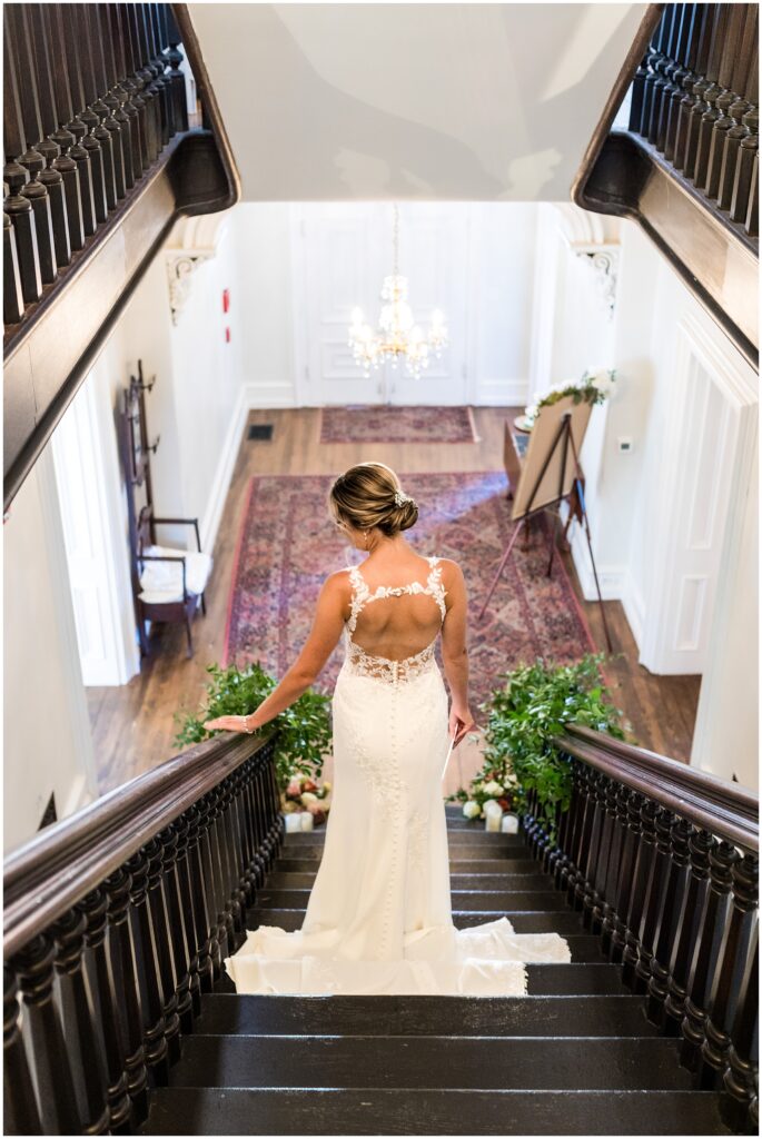 Bride has gorgeous lace details on the back of her wedding dress and descends stairs at Loch Aerie Mansion wedding