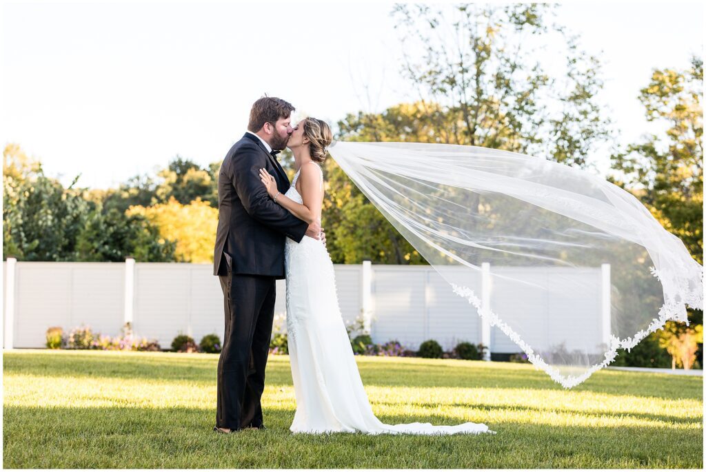 Bride and groom kiss while veil floats behind bride