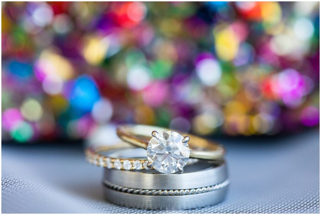 engagement ring and wedding bands with colorful backdrop