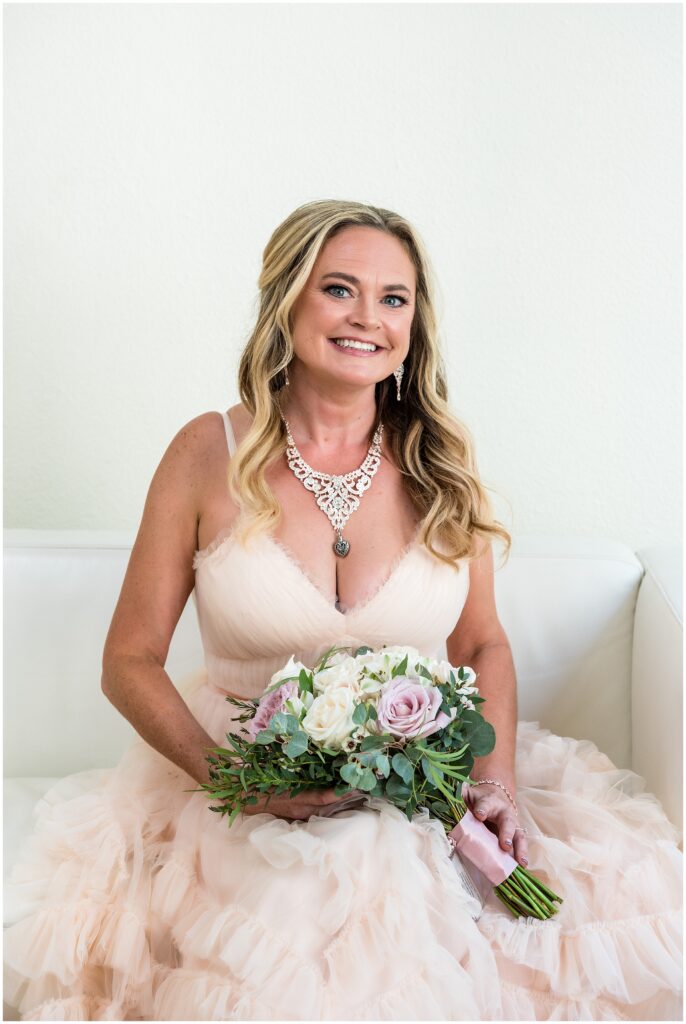 Bride smiles while holding her pink and cream rose bouquet