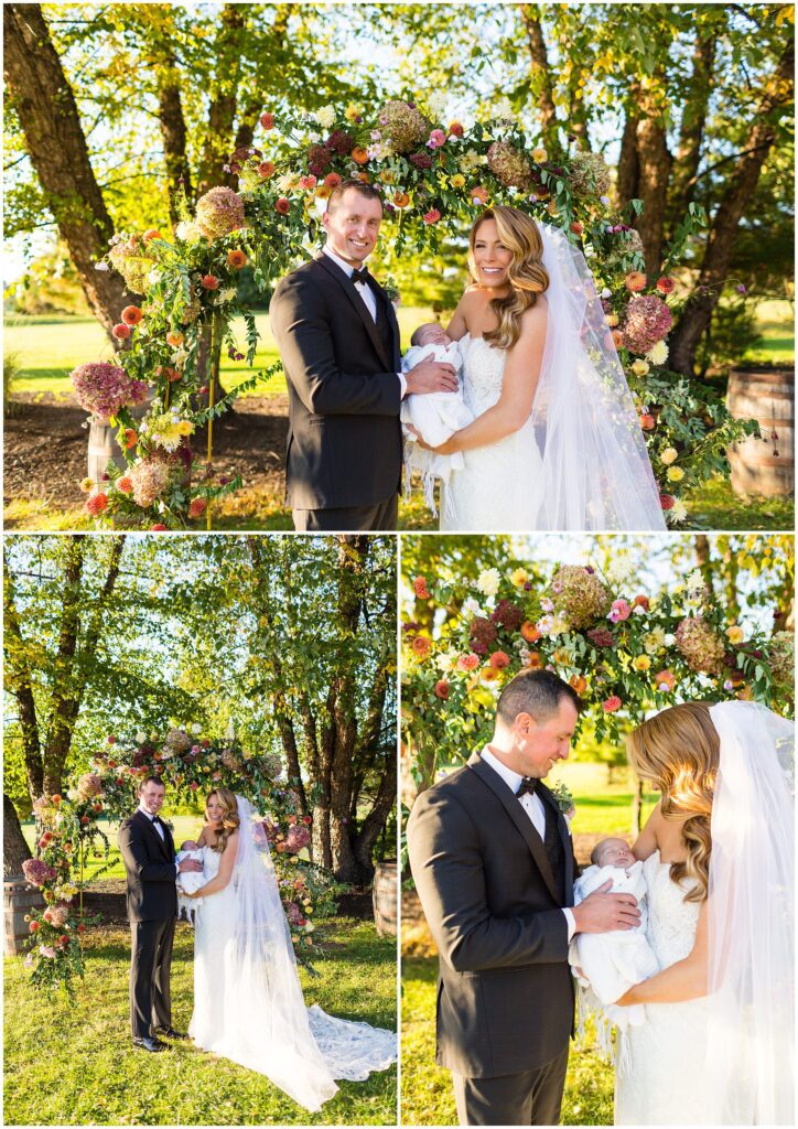 Newlyweds with their newborn, near colorful floral arch