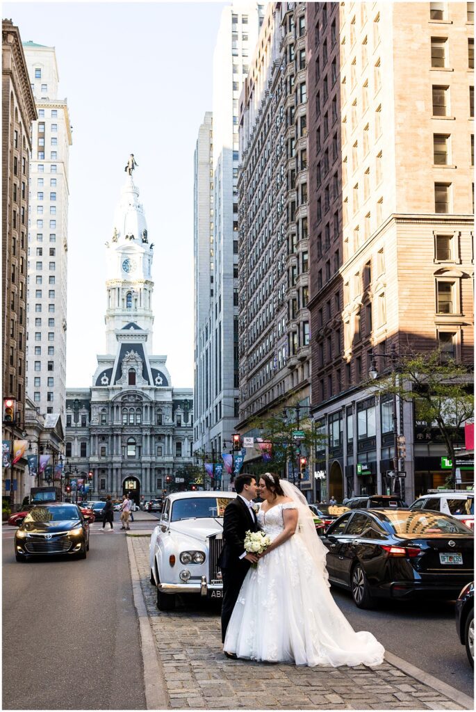 After their ceremony, Bride and Groom pose on Philadelphia's Broad St. with vintage Rolls Royce and City Hall behind them